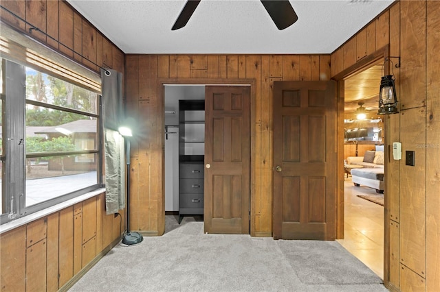 bedroom with a textured ceiling, light colored carpet, ceiling fan, and wood walls