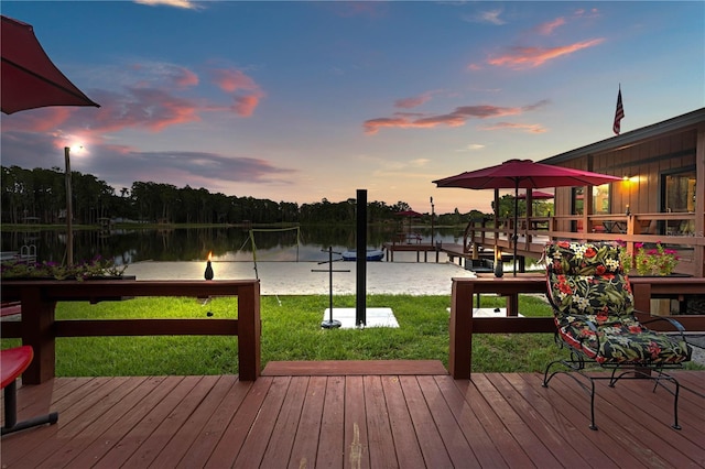 deck at dusk with a water view, volleyball court, and a lawn