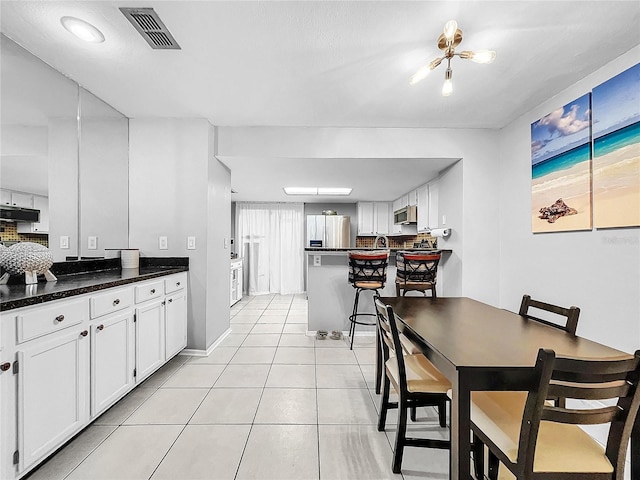 kitchen featuring stainless steel appliances, a kitchen bar, light tile patterned floors, an inviting chandelier, and white cabinets