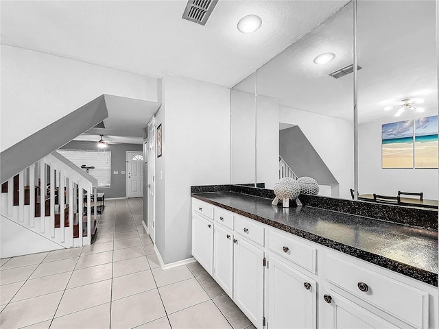 kitchen featuring a textured ceiling, light tile patterned flooring, ceiling fan, white cabinetry, and dark stone countertops