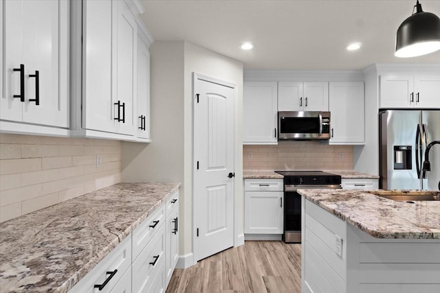 kitchen with white cabinets, appliances with stainless steel finishes, decorative backsplash, hanging light fixtures, and light wood-type flooring