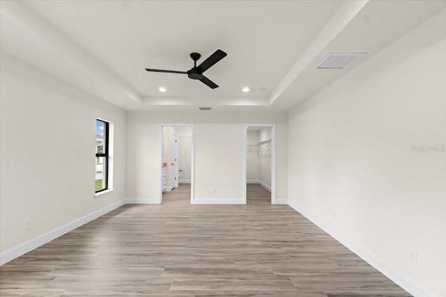 unfurnished bedroom featuring ceiling fan, a tray ceiling, light wood-type flooring, a closet, and a walk in closet