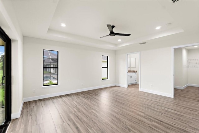 unfurnished bedroom with a raised ceiling, ensuite bath, ceiling fan, and light wood-type flooring