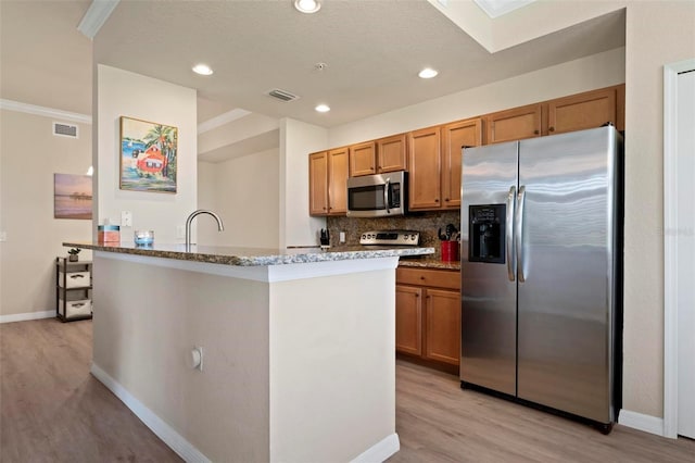 kitchen featuring a skylight, light wood-type flooring, appliances with stainless steel finishes, light stone countertops, and backsplash