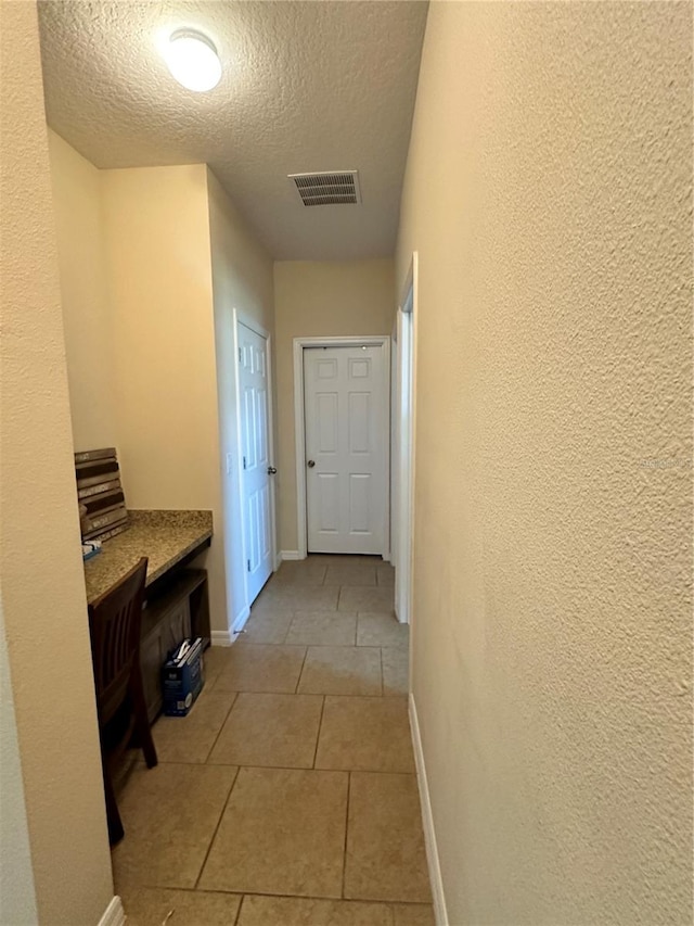 corridor with light tile patterned flooring and a textured ceiling