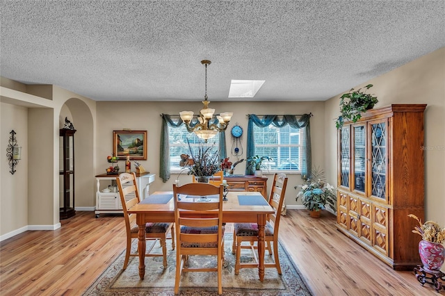 dining area with a skylight, a chandelier, a textured ceiling, and light wood-type flooring