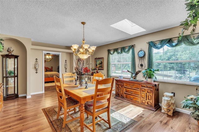 dining room featuring a chandelier, a textured ceiling, a skylight, and light hardwood / wood-style flooring