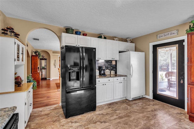 kitchen featuring decorative backsplash, black fridge with ice dispenser, a textured ceiling, white fridge, and white cabinetry