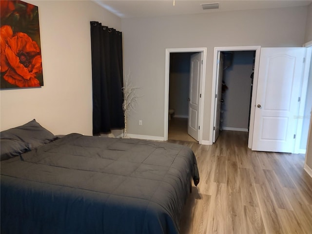 bedroom with ensuite bathroom, light wood-type flooring, a spacious closet, and a closet