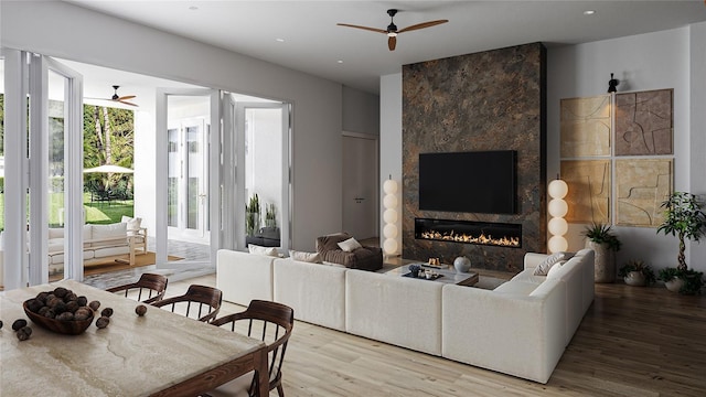 living room with ceiling fan, a large fireplace, and light hardwood / wood-style flooring