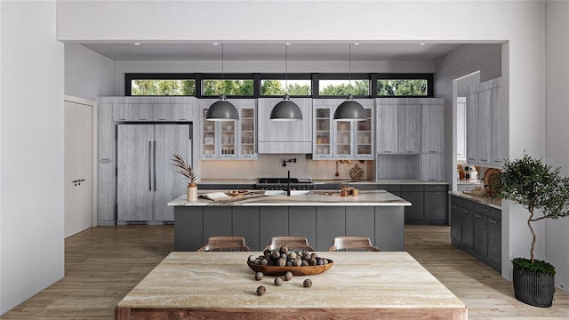 kitchen with paneled refrigerator, light wood-style flooring, a kitchen island, light countertops, and decorative backsplash