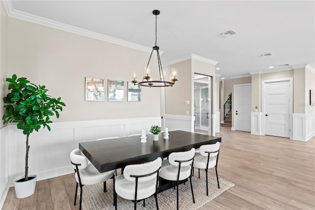 dining space featuring a wainscoted wall, a notable chandelier, visible vents, ornamental molding, and light wood-type flooring