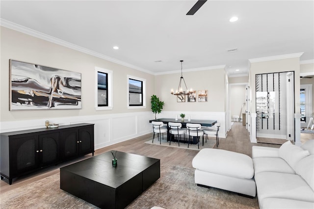 living room with a chandelier, recessed lighting, a wainscoted wall, ornamental molding, and light wood-type flooring