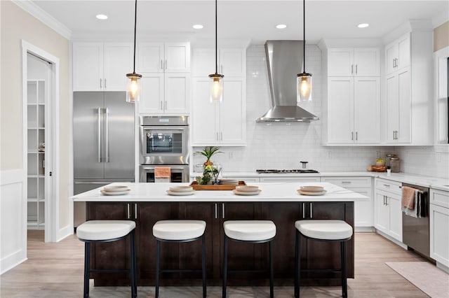 kitchen with appliances with stainless steel finishes, pendant lighting, a kitchen island, and wall chimney range hood