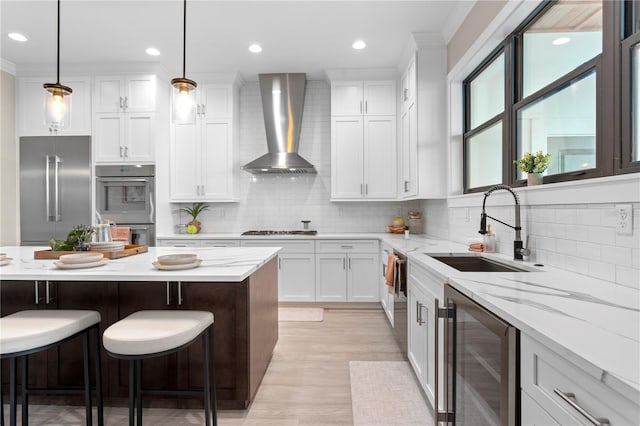 kitchen featuring wine cooler, stainless steel appliances, a sink, white cabinets, and wall chimney range hood