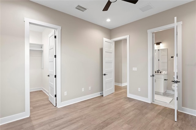 unfurnished bedroom with light wood-type flooring, a walk in closet, visible vents, and baseboards