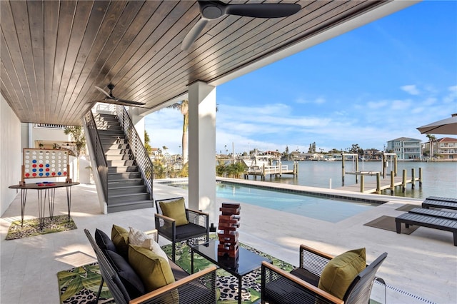 view of patio with a ceiling fan, a water view, an outdoor pool, and stairs