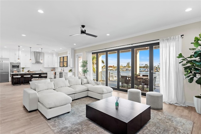 living room featuring a ceiling fan, light wood-style flooring, ornamental molding, a water view, and recessed lighting