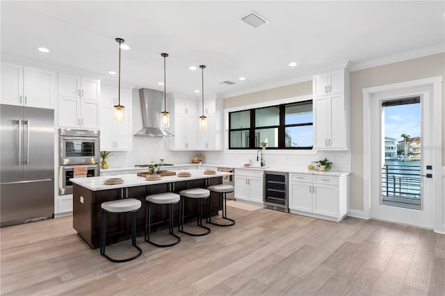 kitchen featuring wine cooler, light countertops, appliances with stainless steel finishes, a center island, and wall chimney exhaust hood