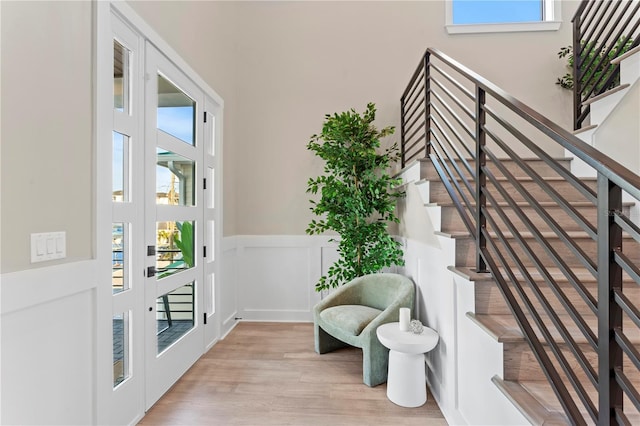 foyer featuring a decorative wall, light wood-style floors, stairs, french doors, and wainscoting