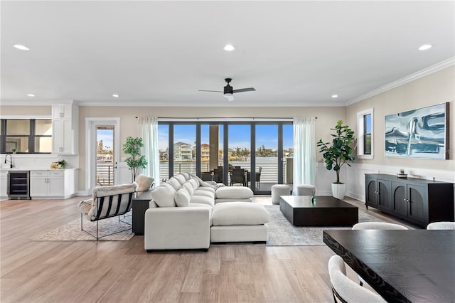 living room with ceiling fan, recessed lighting, beverage cooler, light wood-style floors, and ornamental molding