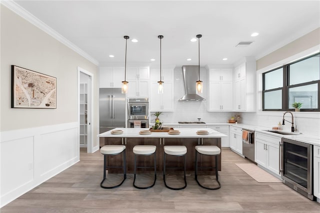 kitchen with wine cooler, a kitchen island, light countertops, wall chimney range hood, and hanging light fixtures