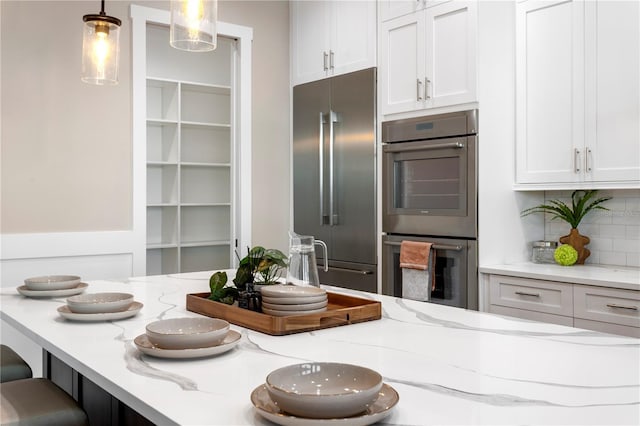 kitchen with decorative light fixtures, decorative backsplash, appliances with stainless steel finishes, white cabinetry, and light stone countertops