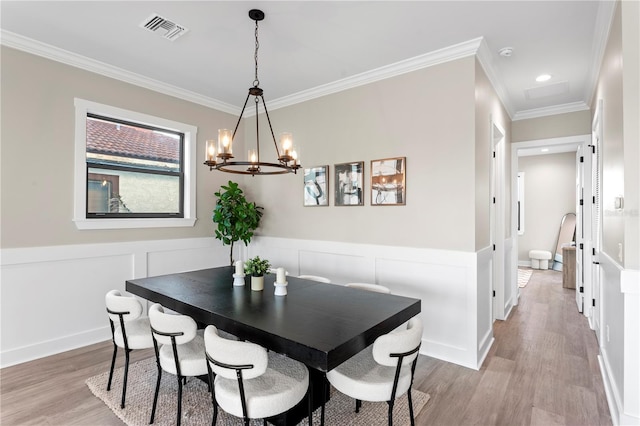 dining space featuring a wainscoted wall, visible vents, a decorative wall, light wood-style flooring, and ornamental molding