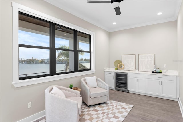 sitting room featuring beverage cooler, a water view, light wood-style flooring, and a healthy amount of sunlight