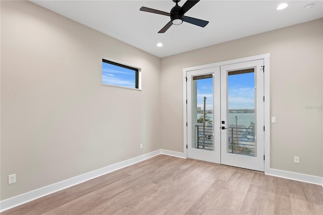 spare room with light wood-style floors, french doors, a water view, and baseboards