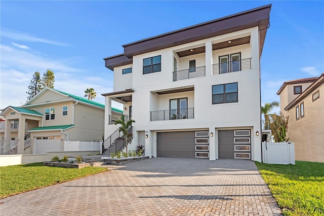 contemporary house featuring decorative driveway, an attached garage, a front yard, and stucco siding