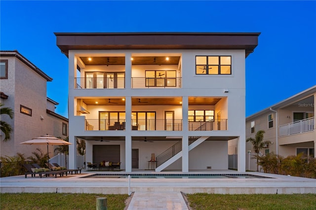 back of house with a balcony, an outdoor pool, stairs, stucco siding, and a patio area