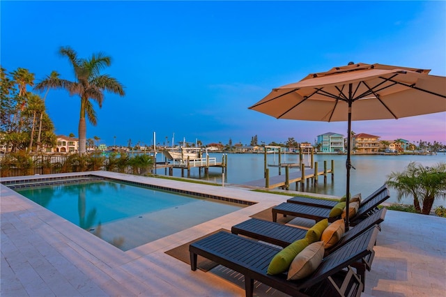 pool at dusk featuring a water view, a boat dock, and boat lift