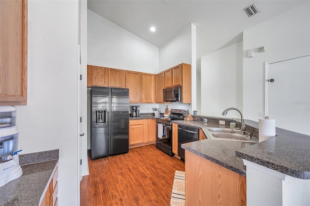 kitchen featuring black appliances, sink, dark hardwood / wood-style floors, a towering ceiling, and kitchen peninsula