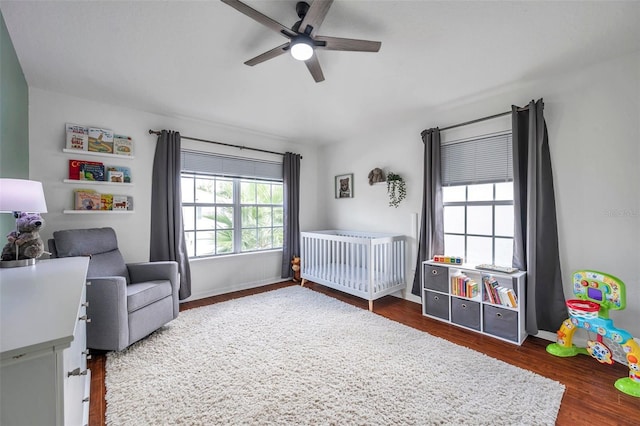 bedroom featuring ceiling fan, dark wood-type flooring, and a nursery area