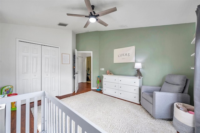 bedroom with hardwood / wood-style floors, ceiling fan, a crib, and a closet