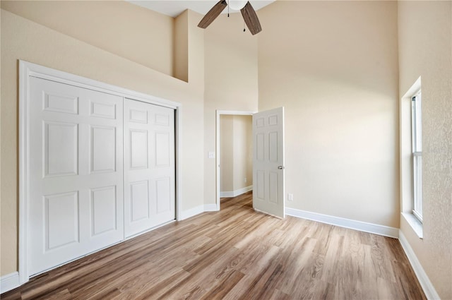 unfurnished bedroom featuring ceiling fan, a closet, a towering ceiling, and light wood-type flooring