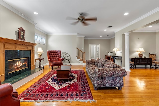 living room with crown molding, decorative columns, a premium fireplace, and light wood-type flooring