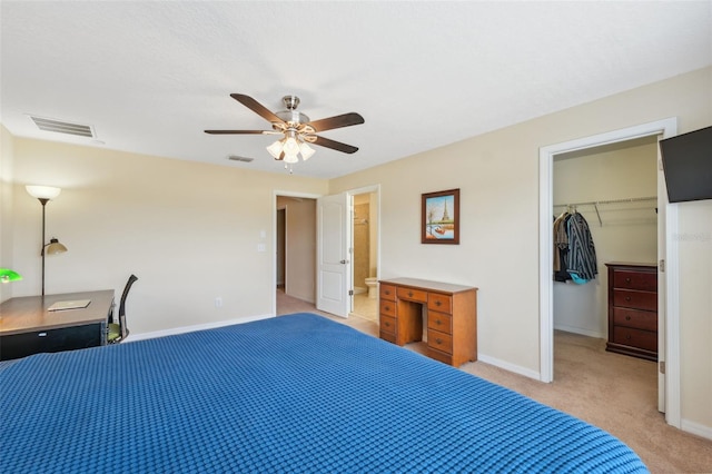 bedroom featuring a spacious closet, connected bathroom, light carpet, a closet, and ceiling fan