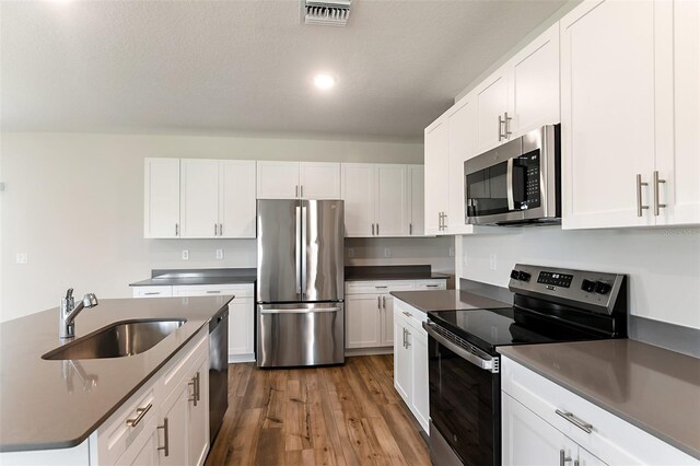 kitchen featuring appliances with stainless steel finishes, wood-type flooring, sink, and white cabinets