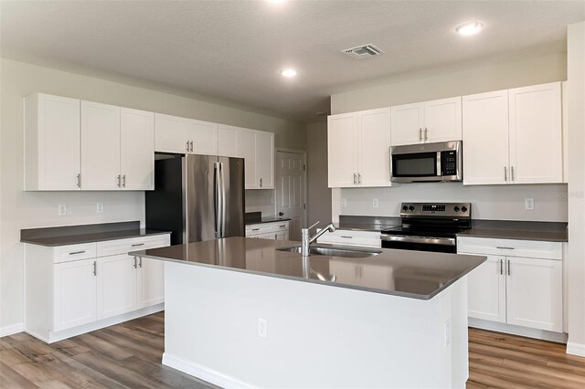 kitchen featuring wood-type flooring, an island with sink, stainless steel appliances, sink, and white cabinetry