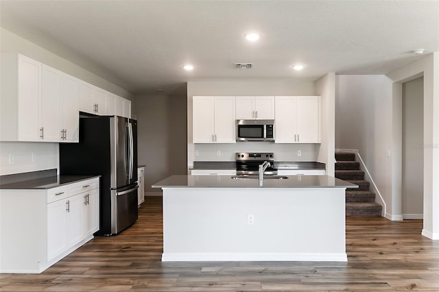 kitchen with dark wood-type flooring, stainless steel appliances, a center island with sink, and white cabinetry