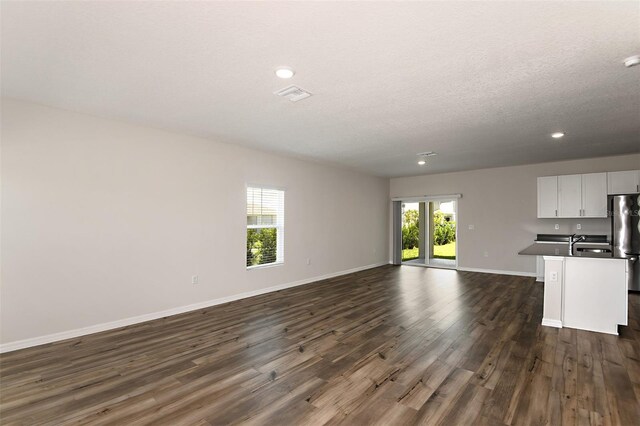 unfurnished living room featuring sink, plenty of natural light, dark hardwood / wood-style flooring, and a textured ceiling