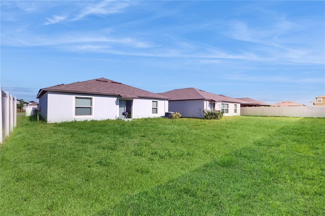 back of house featuring stucco siding, fence, and a lawn