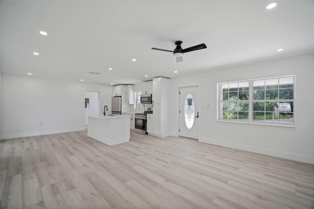 unfurnished living room featuring light wood-type flooring, plenty of natural light, and ceiling fan