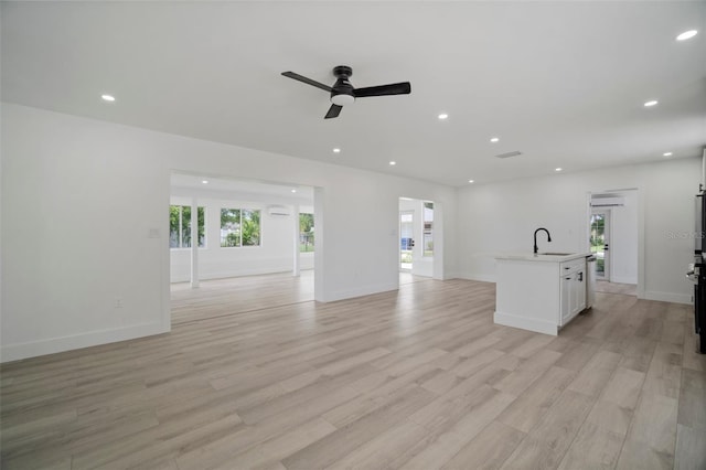 unfurnished living room featuring ceiling fan, light wood-type flooring, sink, and a wealth of natural light