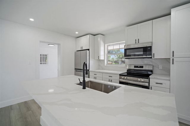 kitchen with light stone counters, white cabinetry, sink, and appliances with stainless steel finishes