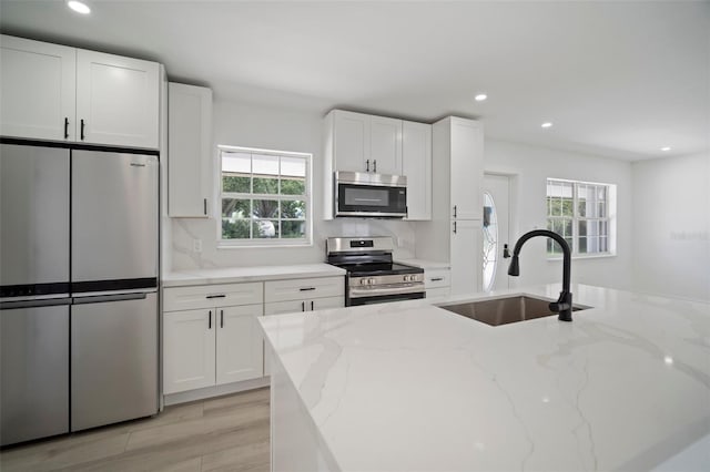 kitchen with light stone countertops, sink, white cabinets, and stainless steel appliances