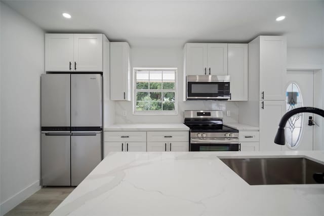 kitchen with appliances with stainless steel finishes, white cabinetry, light stone counters, and sink