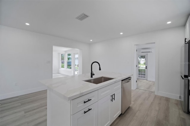 kitchen with a kitchen island with sink, sink, light stone countertops, white cabinetry, and stainless steel appliances